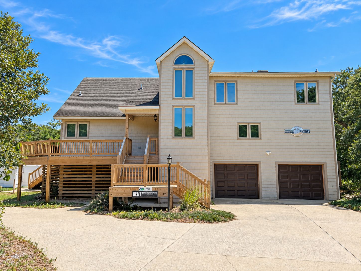 A two-story house with a front deck, a garage, and a sign indicating it is for rent.