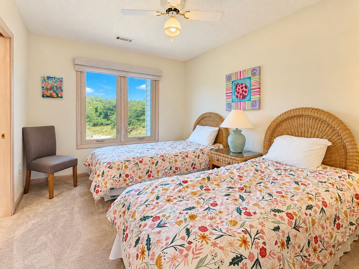 A bedroom with two beds, a chair, a ceiling fan, a window with a view, and artwork on the walls.