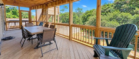 A wooden deck with a table and chairs, large windows, and a view of trees.