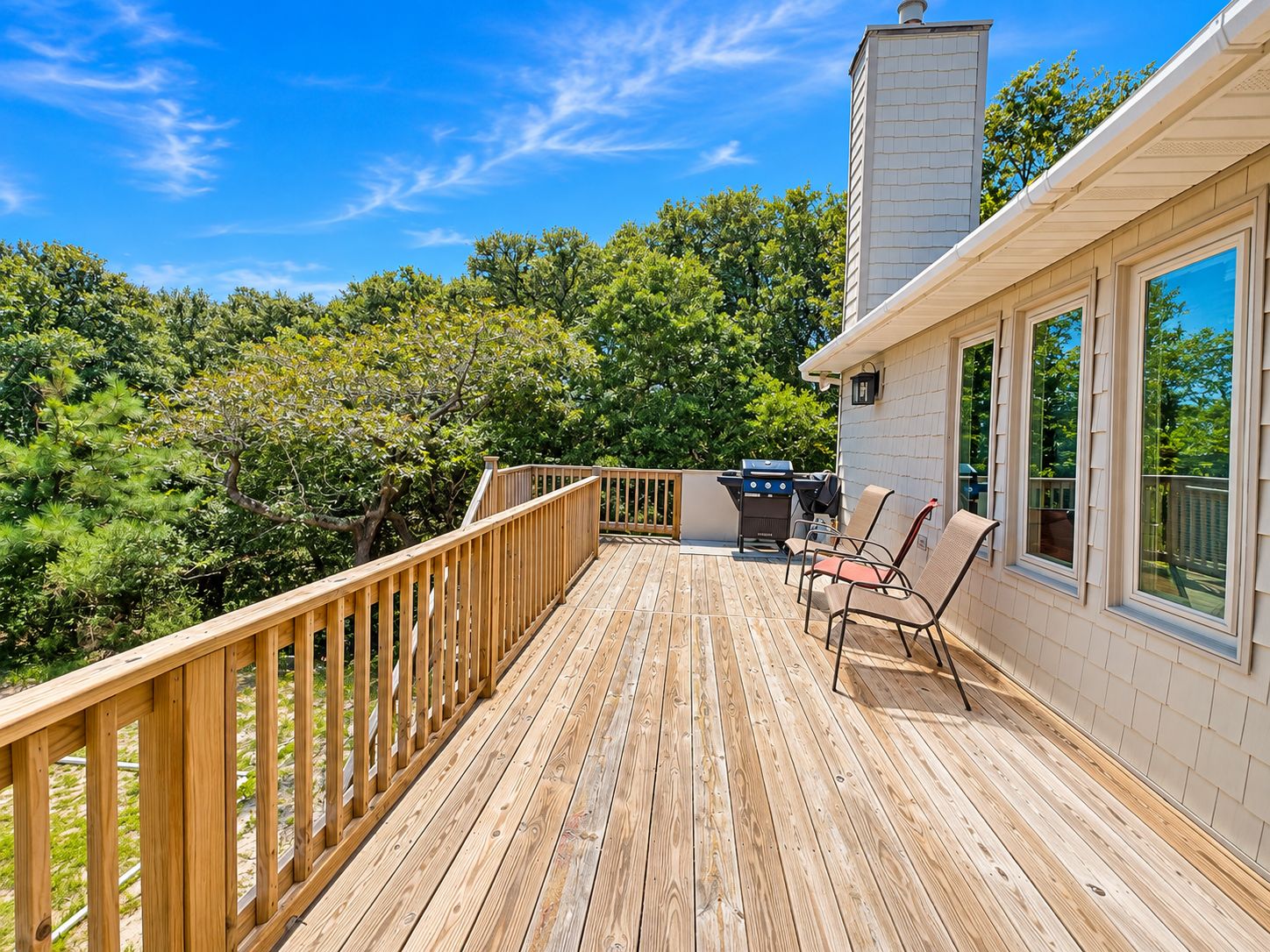 A wooden deck with a railing, a grill, and two chairs.