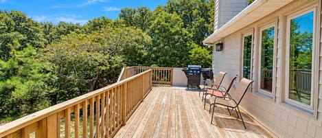 A wooden deck with a railing, a grill, and two chairs.