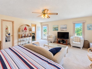 A bedroom with a bed, two chairs, a television, and a ceiling fan. - Carole's Castle - 4 BR Oceanside home in Southern Shores w/Private Pool (Southern Shores)