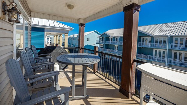 Varanda coberta com cadeiras Adirondack e uma mesa, com vista para uma marina com edifícios azuis.