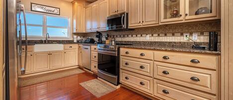A kitchen with wooden cabinets, a stainless steel refrigerator, a microwave, an oven, and a granite countertop.