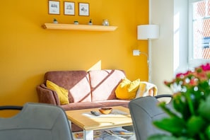 Una sala de estar con una pared amarilla, un sofá marrón con cojines amarillos, una mesa de centro de madera y una lámpara de pie.