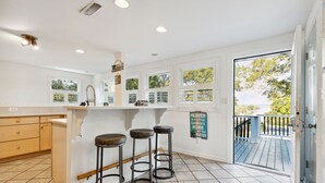 Cozinha com bancada branca, três banquetes e vista para um deck através de uma porta de vidro.