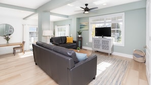 A spacious living room with a dark grey sofa, a television on a white cabinet, and a ceiling fan. - Sandbridge Beach Bay Getaway  (Virginia Beach)