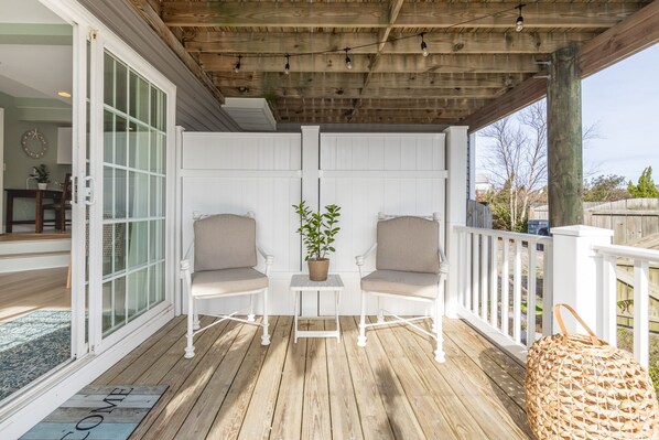 A wooden deck with two white chairs and a potted plant.