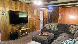 A cozy living room with a large flat-screen TV, a wooden coffee table, and a grey sectional sofa with patterned cushions. - Spacious Family Vacation Retreat! (Packwood)