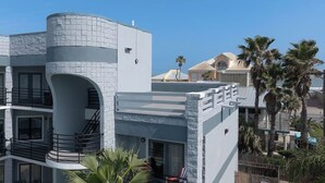 A modern multi-story building with a curved facade, balconies, and a visible sign. - Beachside Bliss • Community Pool • 1 Min Walk to Beach (South Padre Island)