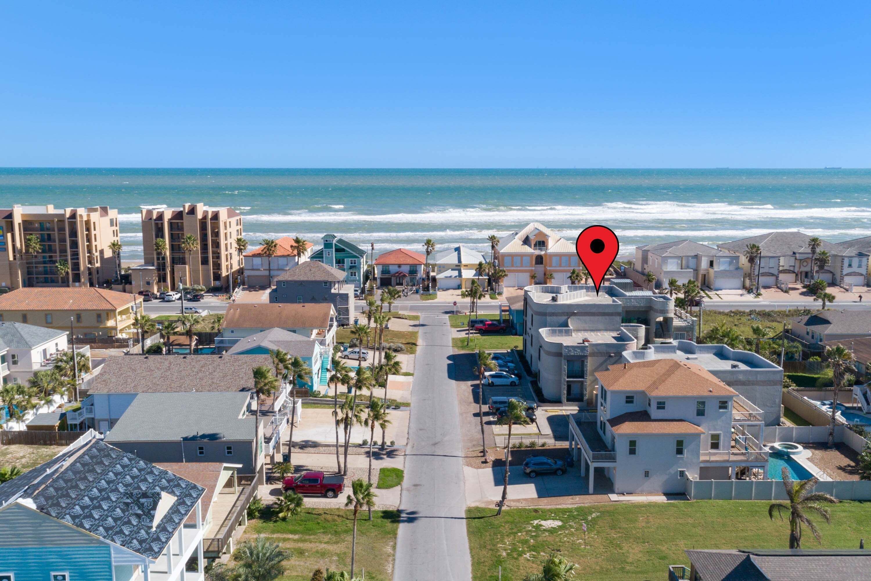 Un quartier résidentiel situé sur la côte, offrant une vue sur l’océan, et comprenant une variété de maisons et d’immeubles, dont une imposante maison blanche dotée d’une piscine.