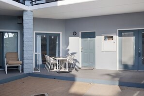 Een overdekt terras met een tafel, stoelen en een stoel, en een deur met de tekst '105'.