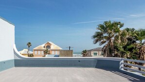 A rooftop terrace with a view of the ocean, palm trees, and buildings in the background. - Beachside Bliss • Community Pool • 1 Min Walk to Beach (South Padre Island)