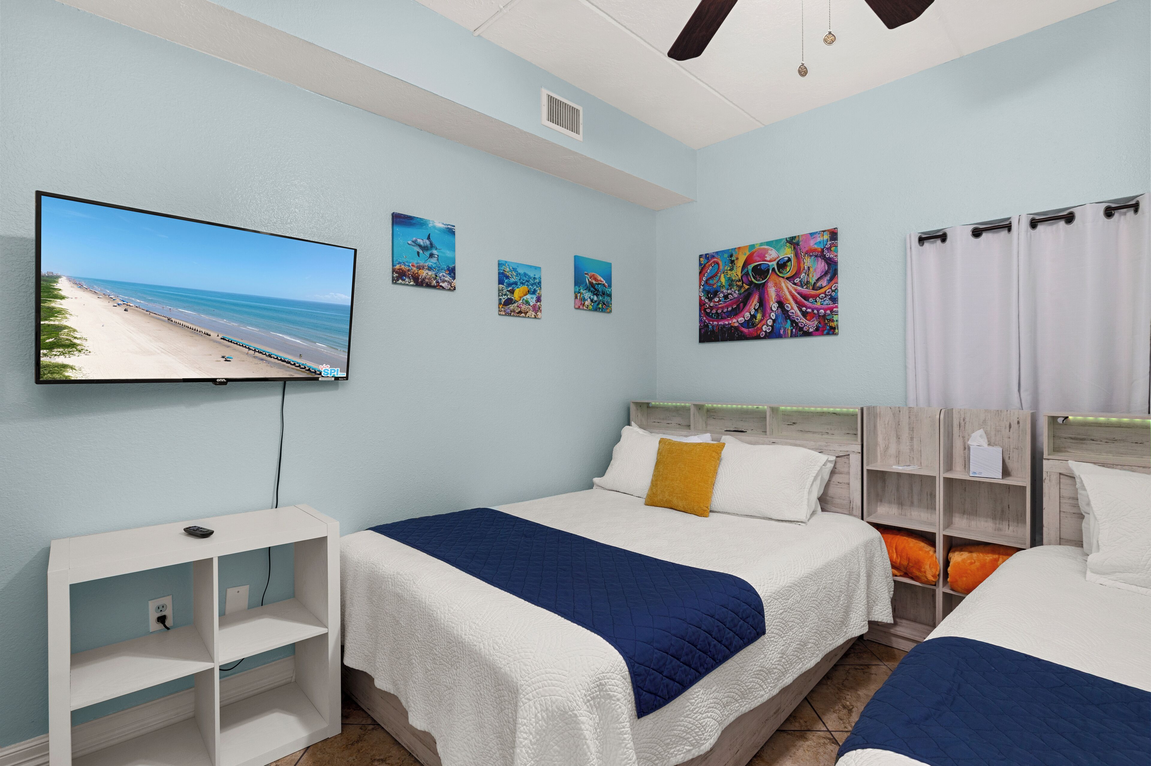 Quarto de hotel com duas camas, uma TV fixada na parede e obras de arte retratando cenas do oceano.