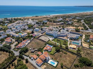 Oversigtsbillede af en kystferie med flere bygninger, en stor swimmingpool og en strand.