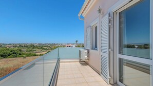 Un balcón con vistas despejadas del paisaje, piso de baldosas y un edificio con ventanas y contraventanas grandes.
