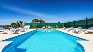 Una piscina rectangular con superficie de agua azul cristalina, rodeada de sillas de descanso a rayas blancas y azules.
