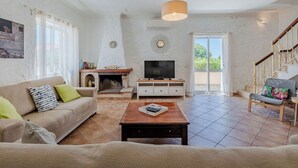 Una sala de estar con chimenea, sofá, mueble para televisión y una escalera.