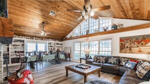 A spacious living room with a high ceiling, wooden beams, a leather sofa, a coffee table, and a dining area with a table and chairs. - Family Friendly Farm House- 10 minutes from WEC (Ocala)
