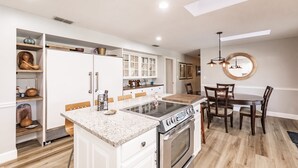 A modern kitchen with white cabinetry, a central island, and a dining area with wooden chairs. - Family Friendly Farm House- 10 minutes from WEC (Ocala)