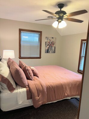 Una camera da letto con un letto, una ventola a soffitto, una finestra con persiane e un quadro appeso al muro.