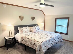 Une chambre à coucher comprenant un lit, deux lampes fixées au mur, un ventilateur de plafond et une fenêtre avec des stores.