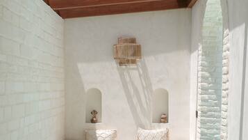 A spa area with a wooden ceiling, white brick walls, a small seating area with cushions, and a pool.