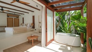 A modern bedroom with a large bed, a sofa, a small table, and a ceiling fan. - Breathe Boutique (Pecatu)