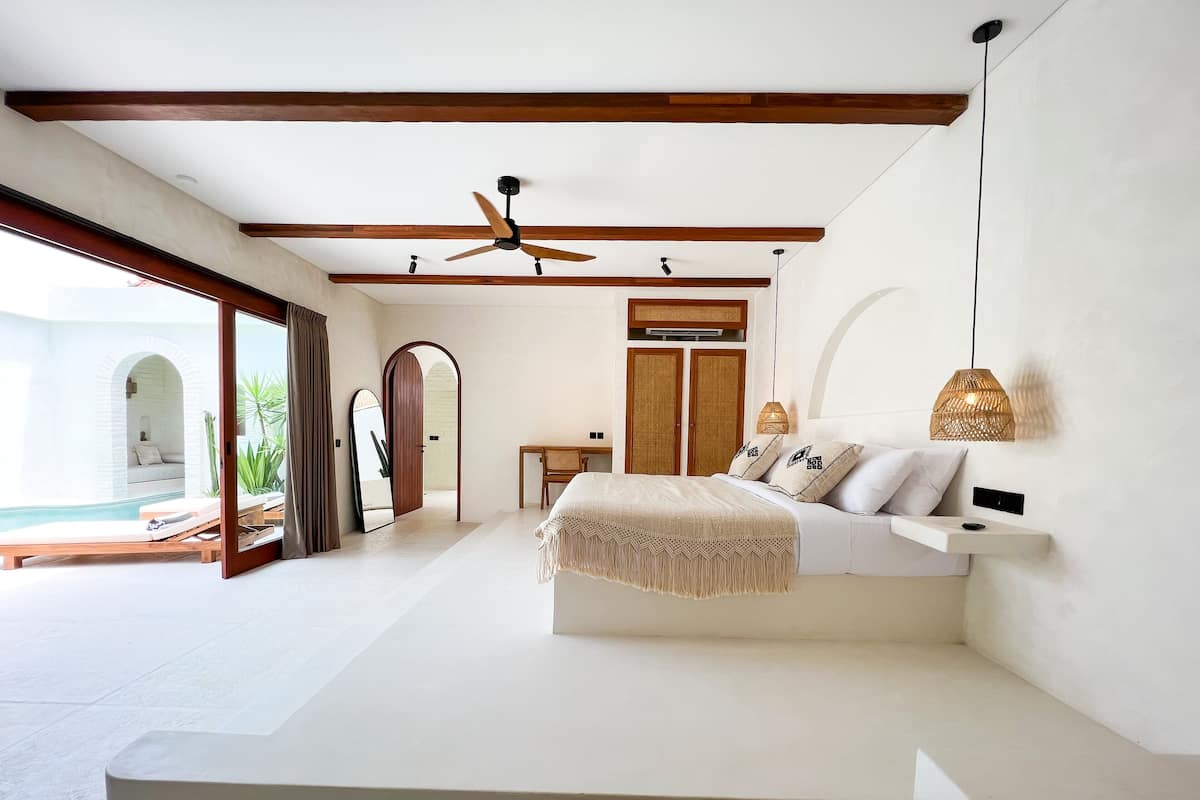 A spacious bedroom with a large bed, a ceiling fan, and a view of a swimming pool.