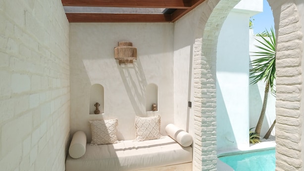 A pool area with a white brick wall, wooden beams, and a seating area with cushions. - Breathe Boutique (Pecatu)