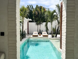A swimming pool with two sun loungers and a door leading to a covered area. - Breathe Boutique (Pecatu)