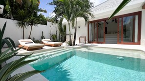 A swimming pool with lounge chairs, surrounded by tropical plants and a modern house with large glass doors. - Breathe Boutique (Pecatu)