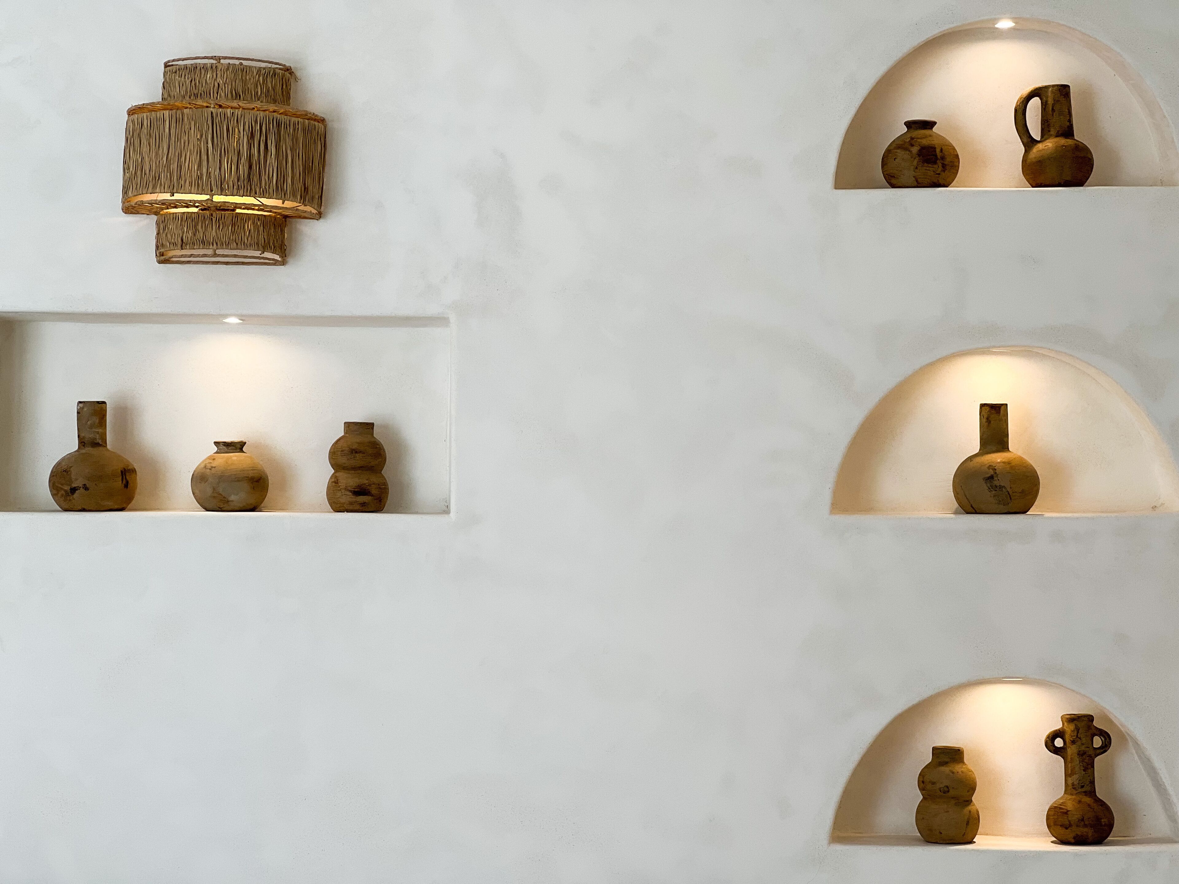 A wall with multiple shelves displaying various ceramic vases.