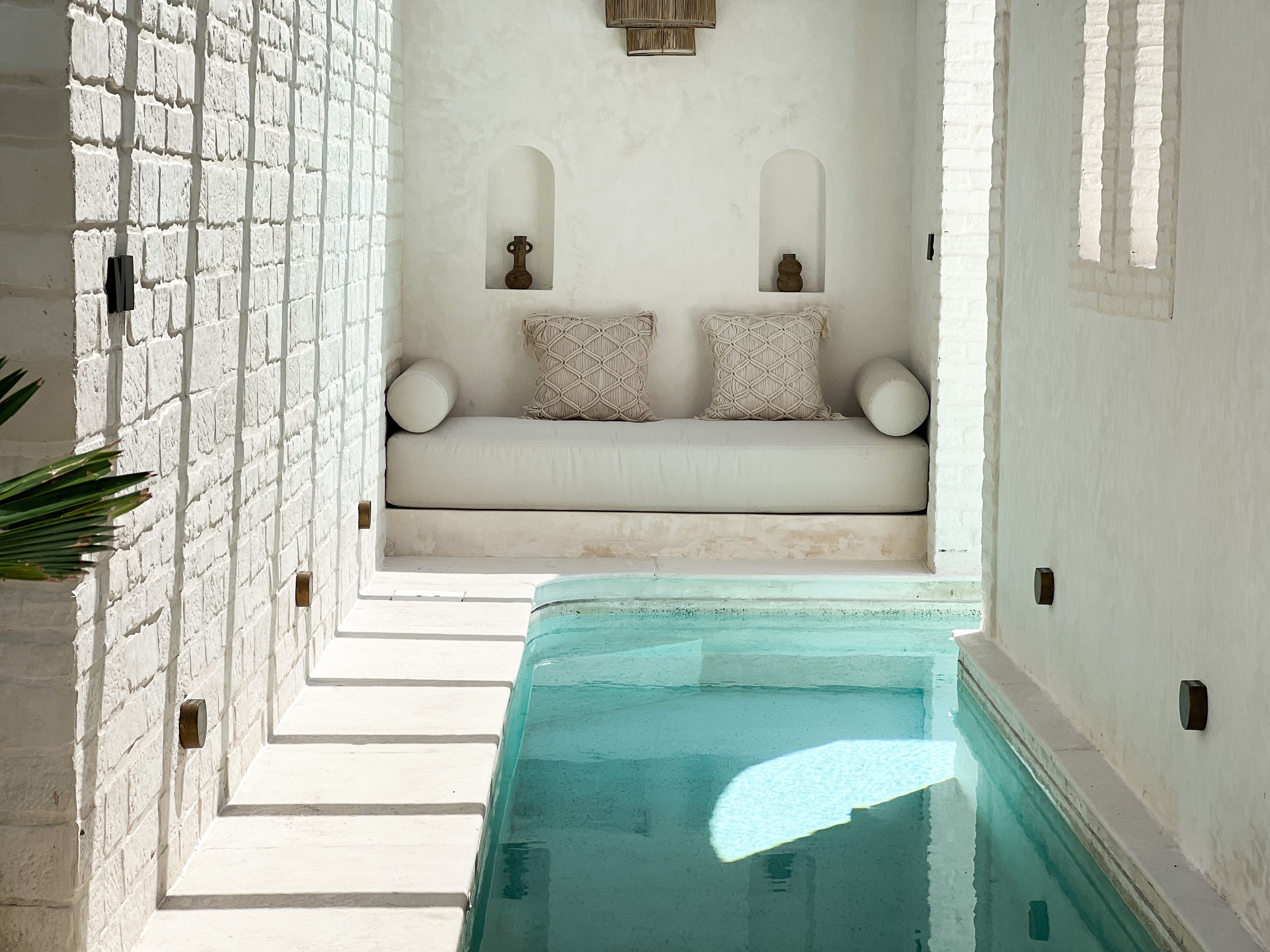 A spa area with a white brick wall, a seating area with cushions, and a pool.