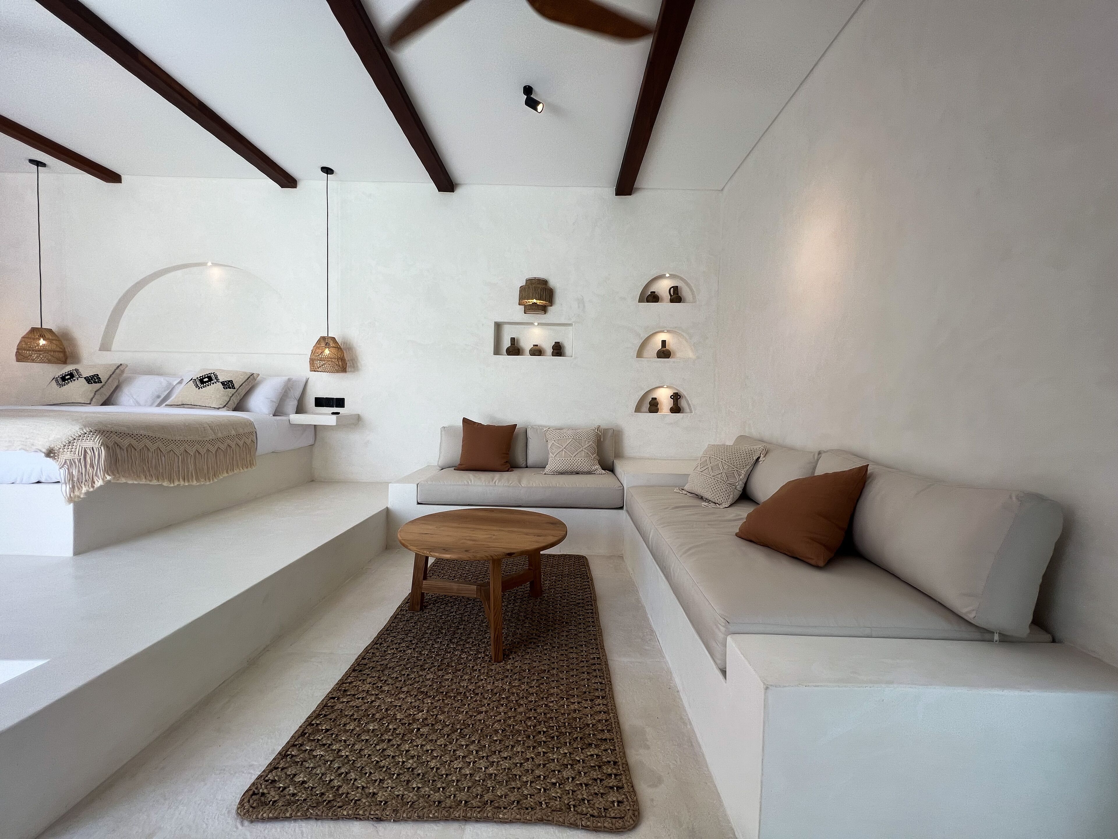Uma sala de estar moderna com um sofá, uma mesa de centro e um tapete. Há prateleiras fixadas na parede com objetos decorativos.