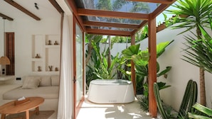 A modern living room with a sofa, a wooden coffee table, and a glass-enclosed hot tub. - Breathe Boutique (Pecatu)