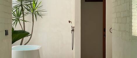 Un baño minimalista con una bañera blanca grande, zona de ducha y una planta en maceta.