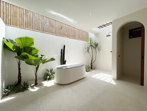 Bathroom features a large bathtub, bamboo wall panel, and potted plants.