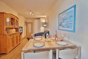 Un coin repas avec un buffet en bois, une table dressée pour quatre personnes et un tableau encadré accroché au mur.