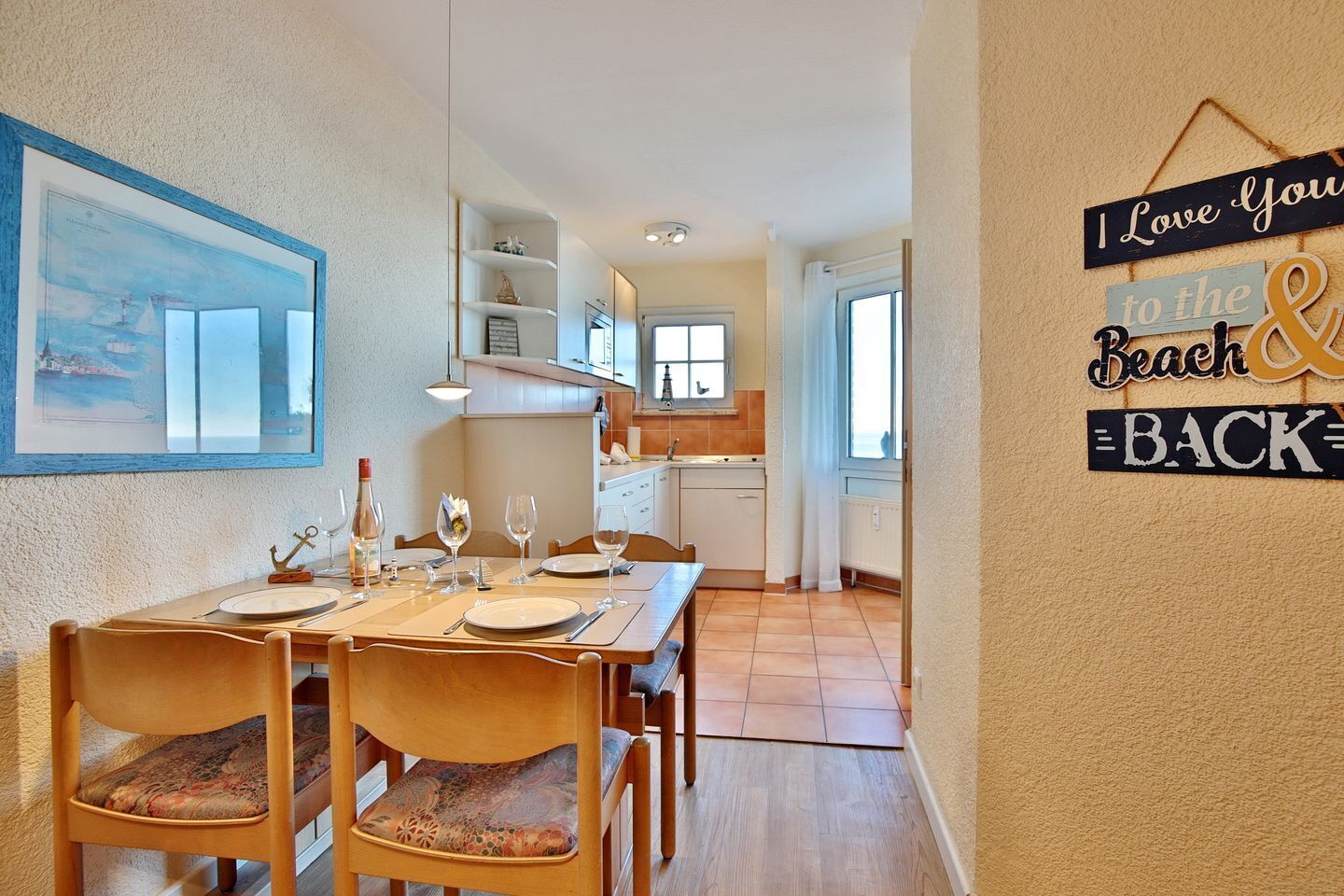 Ein Essbereich mit Tisch für vier Personen, eine Küche im Hintergrund und eine Wand mit dem Schild 'I Love you to the Beach & Back'.