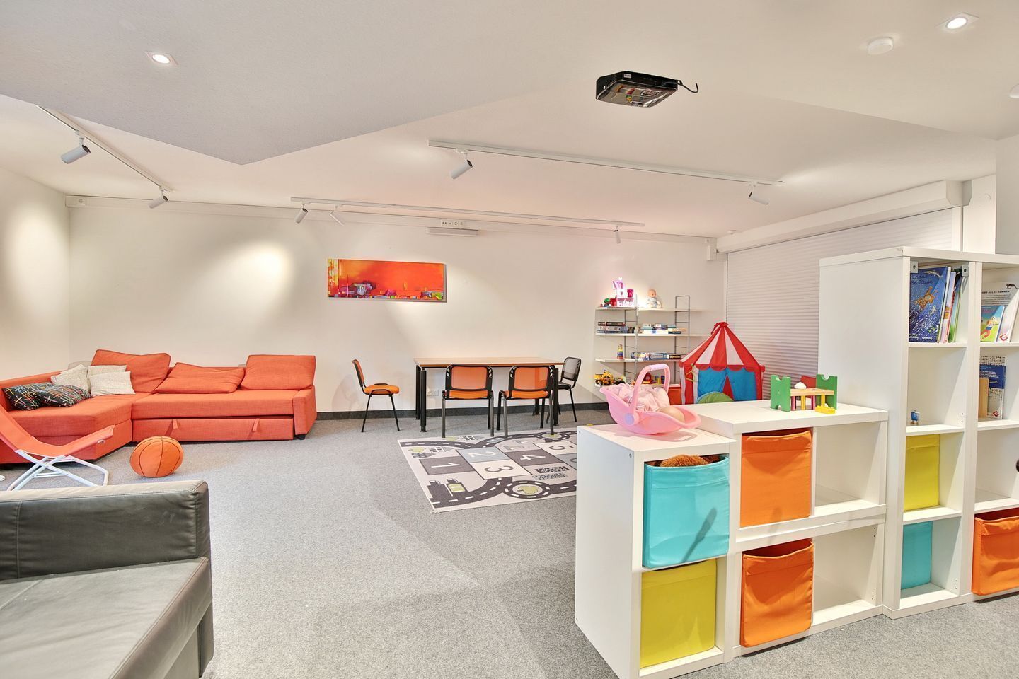 A modern living room with a sectional sofa, a dining table, and a bookshelf.