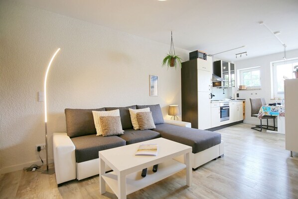 A modern living room with a sofa, a coffee table, and a kitchen in the background.