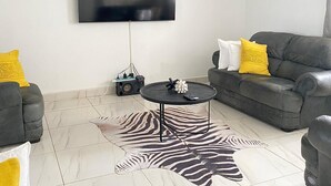 A modern living room with a flat-screen TV, two grey sofas with yellow cushions, a zebra-patterned rug, and a unique pendant light. - The View - Heights, Kariba  (kariba)