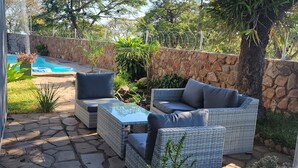 A patio area with wicker furniture, a stone wall, and a pool in the background. - The View - Heights, Kariba  (kariba)