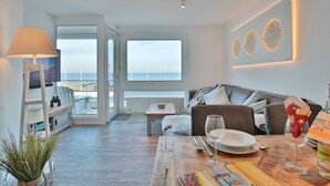Una sala de estar moderna con un sofá, una mesa de comedor con platos y vasos, y un amplio ventanal con vistas al mar.