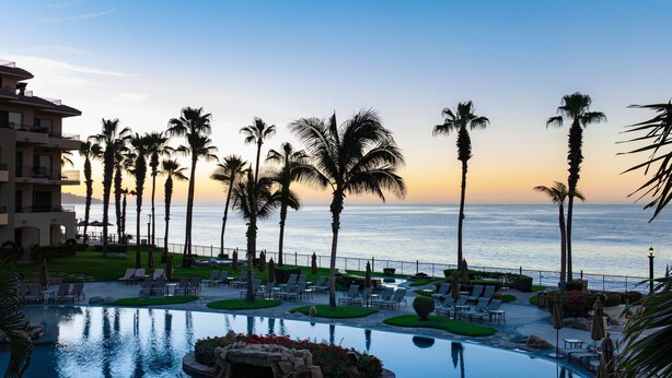 A resort with a pool, lounge chairs, palm trees, and a view of the ocean. - Medano Beachfront Resort-Luxury Villa Overlooking Pool and Sea of Cortez! (Cabo San Lucas)