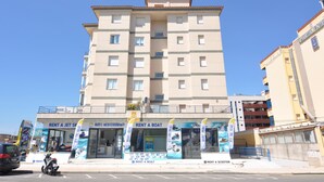 Un immeuble à plusieurs étages, avec une enseigne indiquant « LOCATION D’APPARTEMENTS » et un magasin proposant des services de location de bateaux.