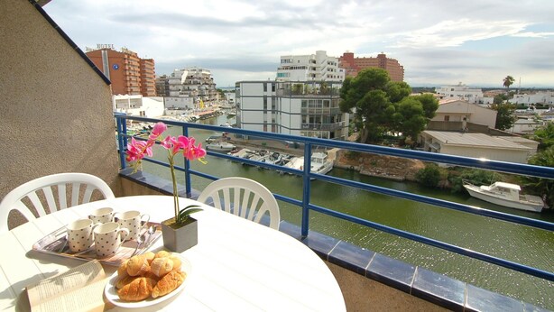 Un balcon avec une table préparée pour le petit-déjeuner, offrant une vue sur un port de plaisance et le paysage urbain.