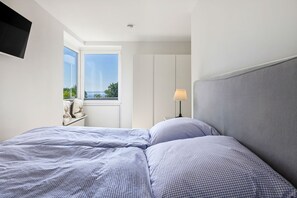 Ein Schlafzimmer mit Bett, Nachttisch, Lampe und einem Fenster mit Blick.