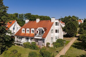 Ein zweigeschossiges Haus mit rotem Ziegeldach, zahlreichen Fenstern und einem sichtbaren Balkon.